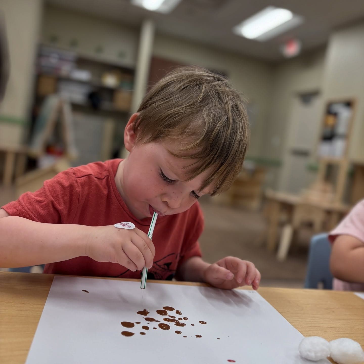 Preschool student using a straw to create bubble paint artwork, strengthening breath control, creativity, and fine motor skills during a hands-on classroom activity.