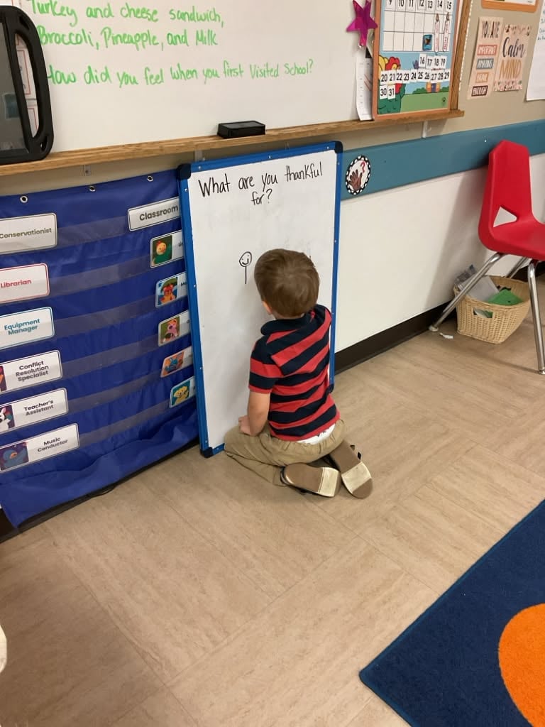 Preschool student writes on a classroom whiteboard during a reflective learning activity that encourages communication and early writing skills at Primrose School.