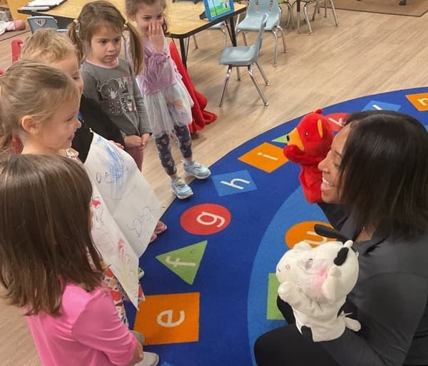 A teacher using a cow puppet to talk to 5 children