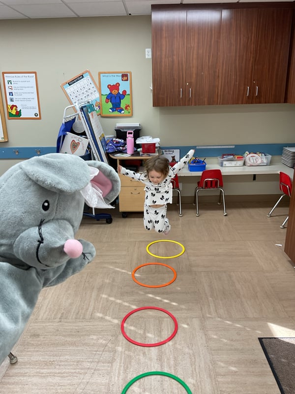 Young child practicing balance, coordination, and gross motor skills by jumping through colorful hoops during an indoor movement activity.