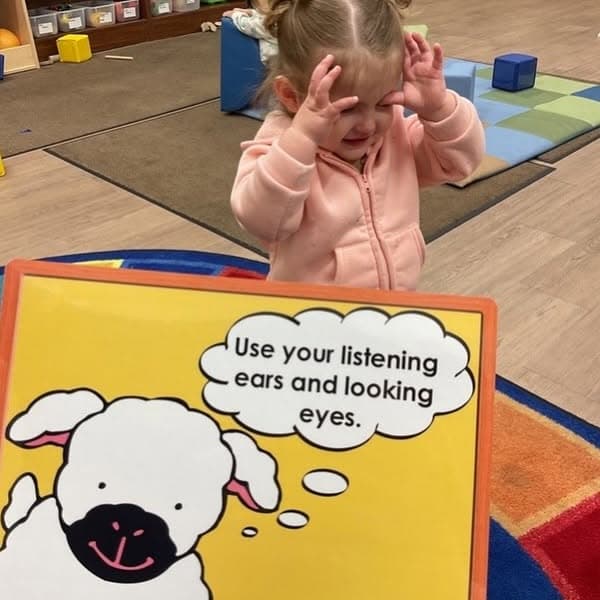 Toddler participating in a classroom lesson about listening and attention skills while learning social-emotional concepts through interactive activities.