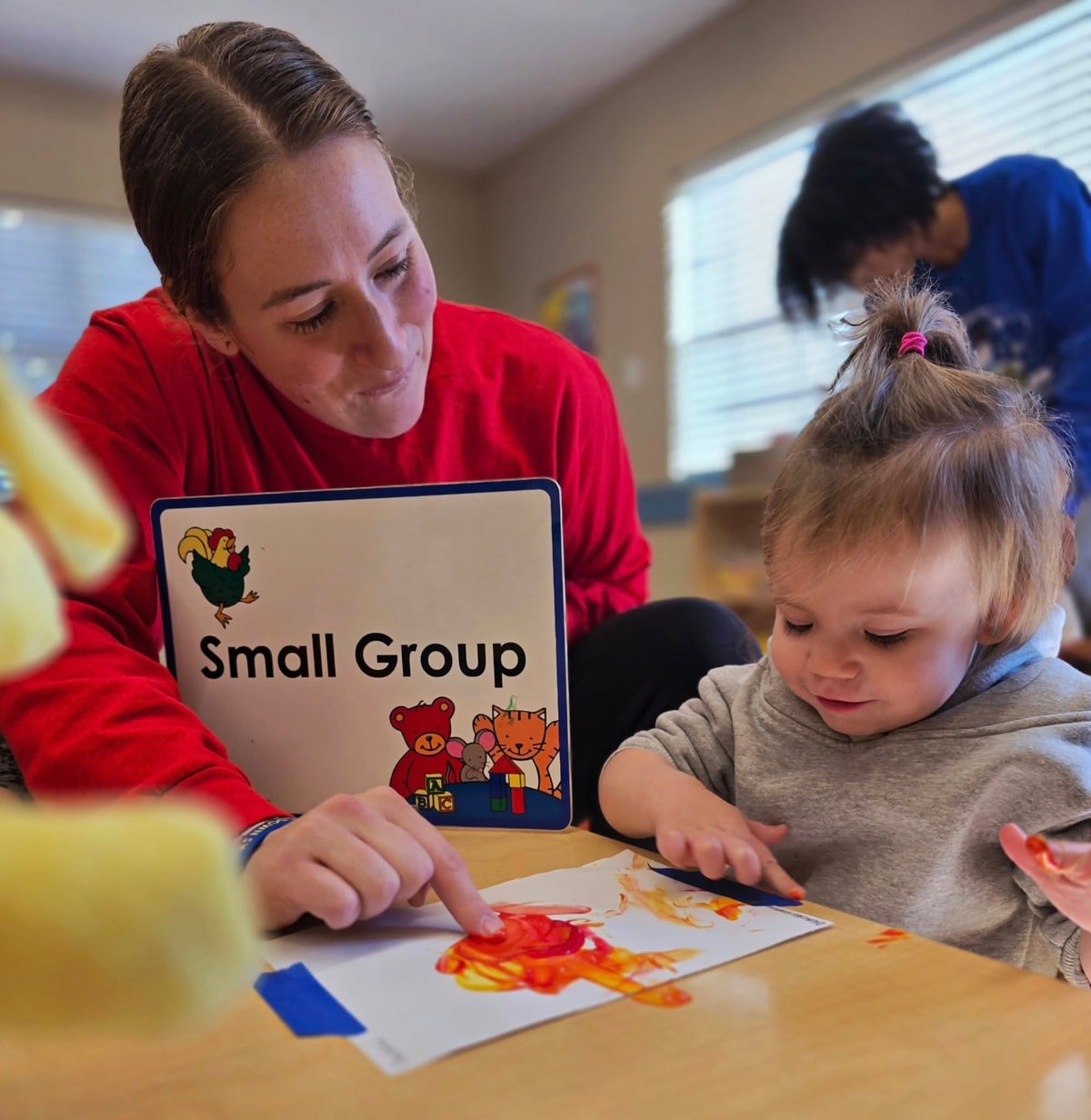 Teacher helping a child during a small group art project, guiding creativity and fine motor skills in an early learning classroom located in Fort Worth, TX.