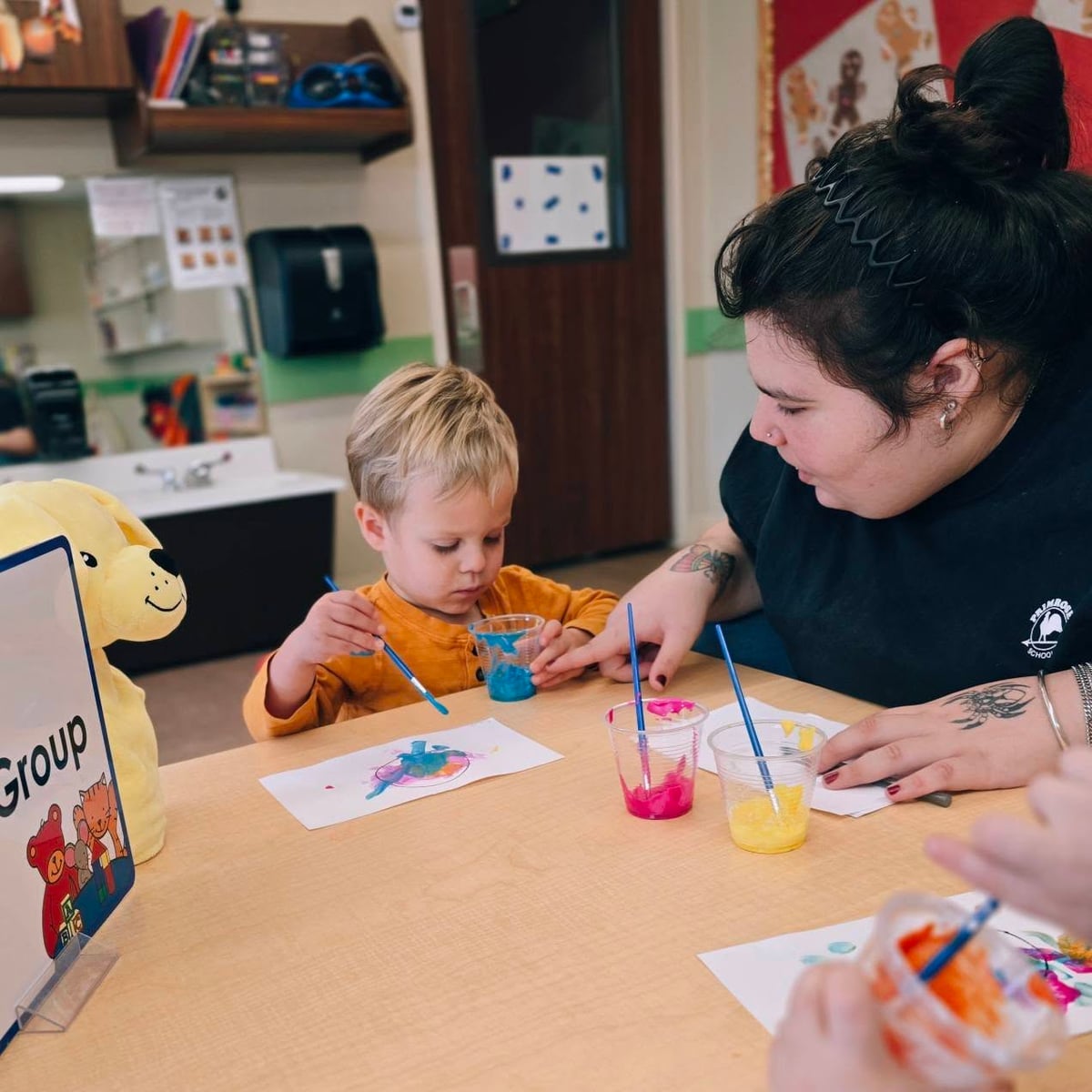 Teacher helping a child during a small group art project, guiding creativity and fine motor skills in an early learning classroom located in Fort Worth, TX.