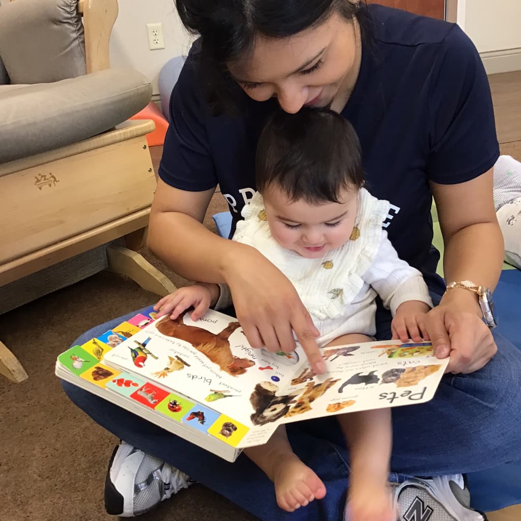 Primrose Fort Worth infant teacher reading a board book about animals with a baby during early literacy time. Best infant care near me