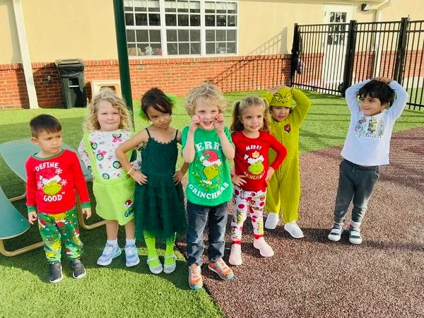 Seven kids in green and red grinch outfits standing outside