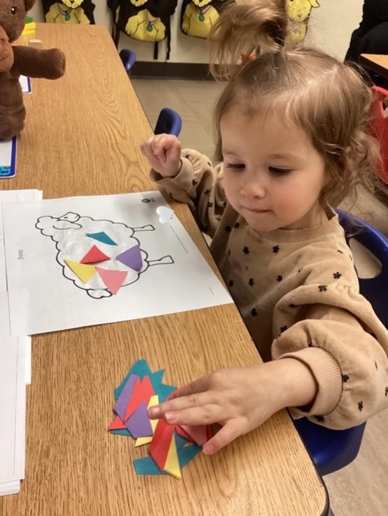 Toddler placing colorful geometric shapes onto a sheep-themed activity sheet while practicing shape recognition and fine motor skills.