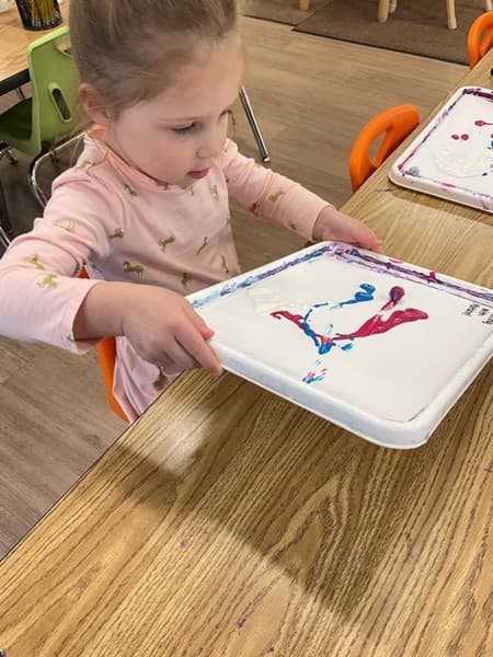 A girl rolling a marble in paint to create a painting
