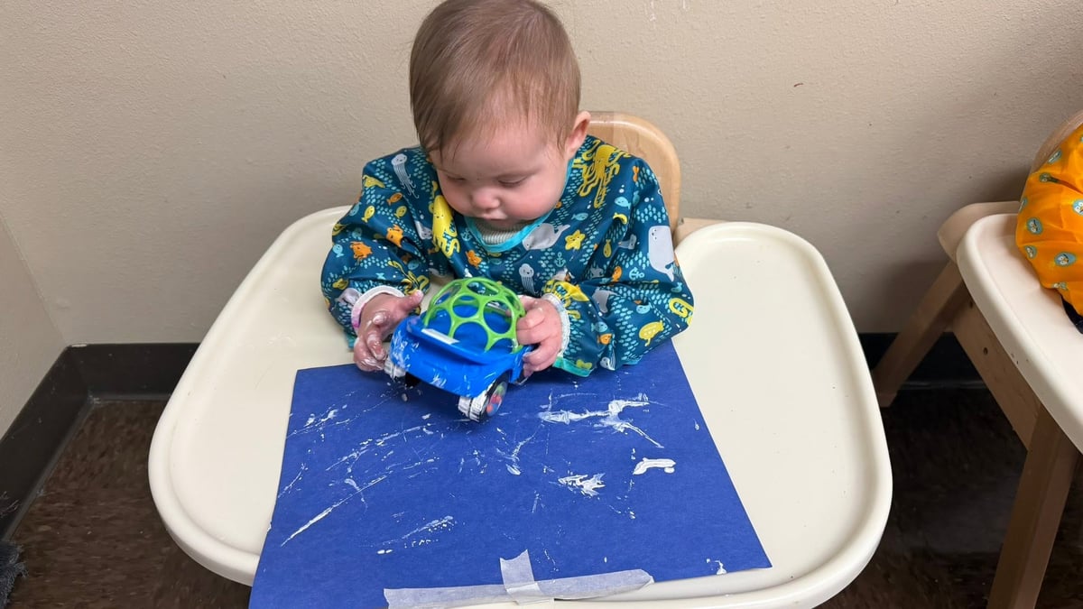 Infant creating a process art painting by rolling a toy car through paint, building fine motor skills, sensory exploration, and creativity at Primrose School.
