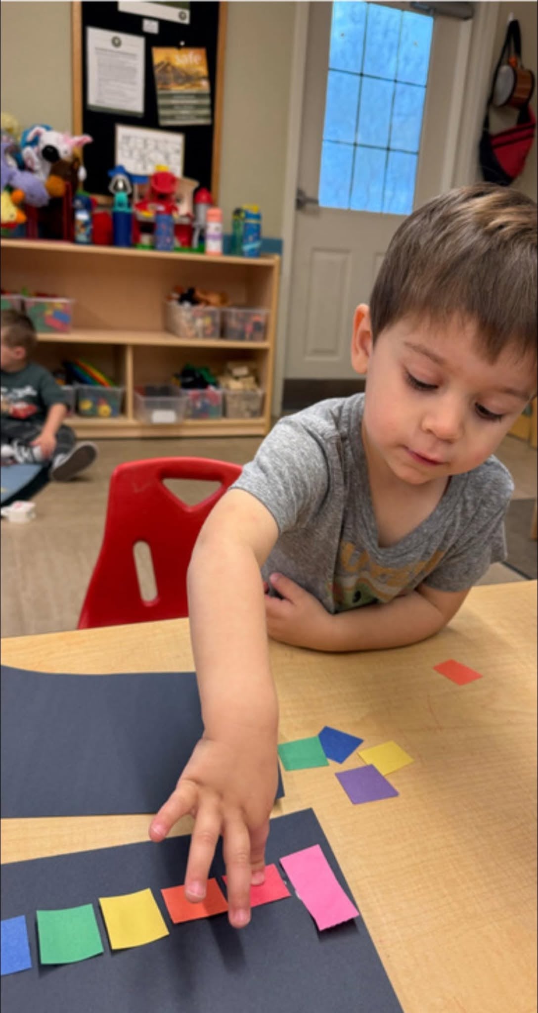 Preschooler arranging colorful paper squares during a classroom activity that builds color recognition, patterning, and fine motor skills at Primrose School.