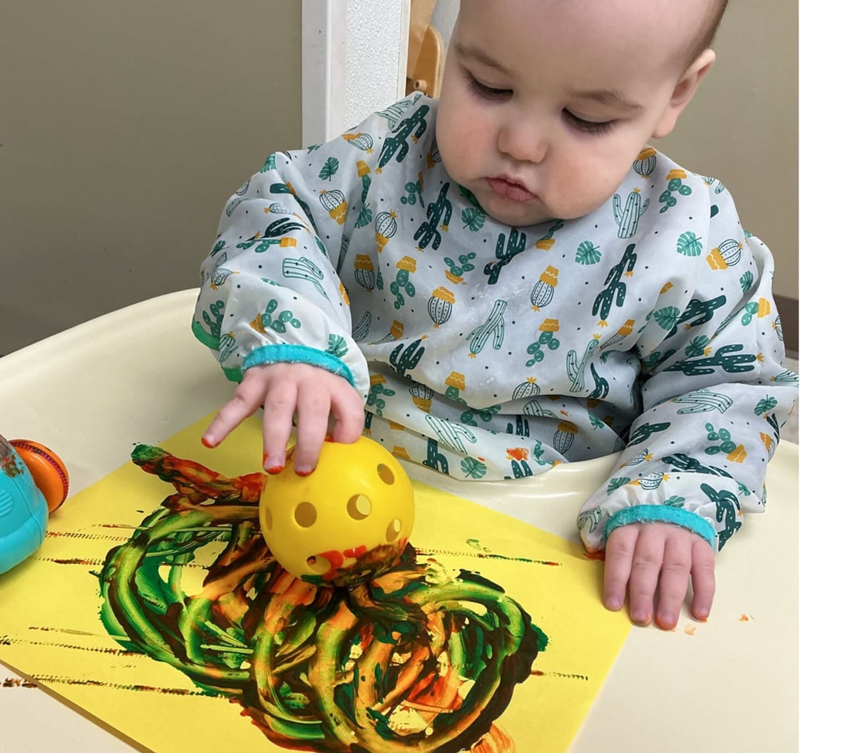 Infant rolling a textured ball through paint to create colorful artwork during a sensory-rich process art activity that supports creativity and fine motor development at Primrose School.