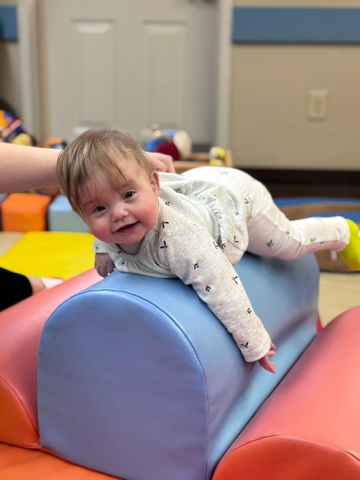 Smiling infant practicing tummy time on soft play equipment to strengthen core muscles, balance, and early mobility skills at Primrose School.
