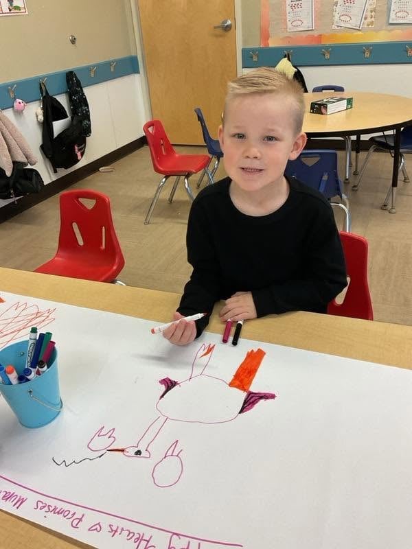 Preschool student proudly displays a Thanksgiving-themed drawing created during a classroom art activity at Primrose School.