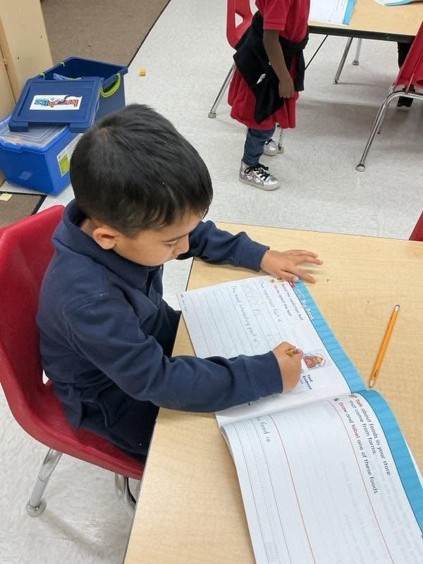 Pre-K student completing a writing activity in a workbook to strengthen handwriting, sentence formation, reading comprehension, and early literacy skills at Primrose School.