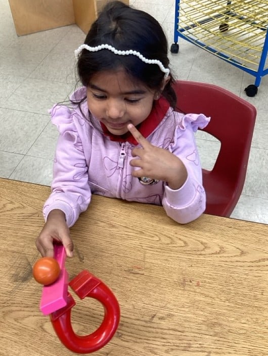 Preschool student investigating magnetism by using a horseshoe magnet during a hands-on STEM learning activity.