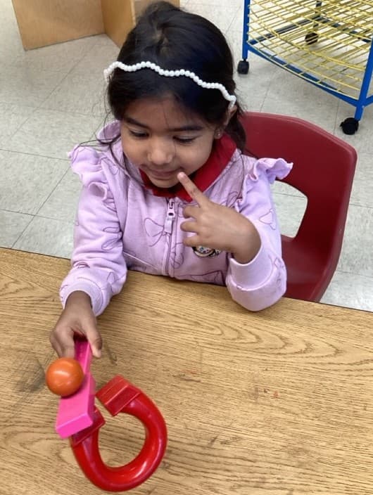 Preschool student investigating magnetism by using a horseshoe magnet during a hands-on STEM learning activity.