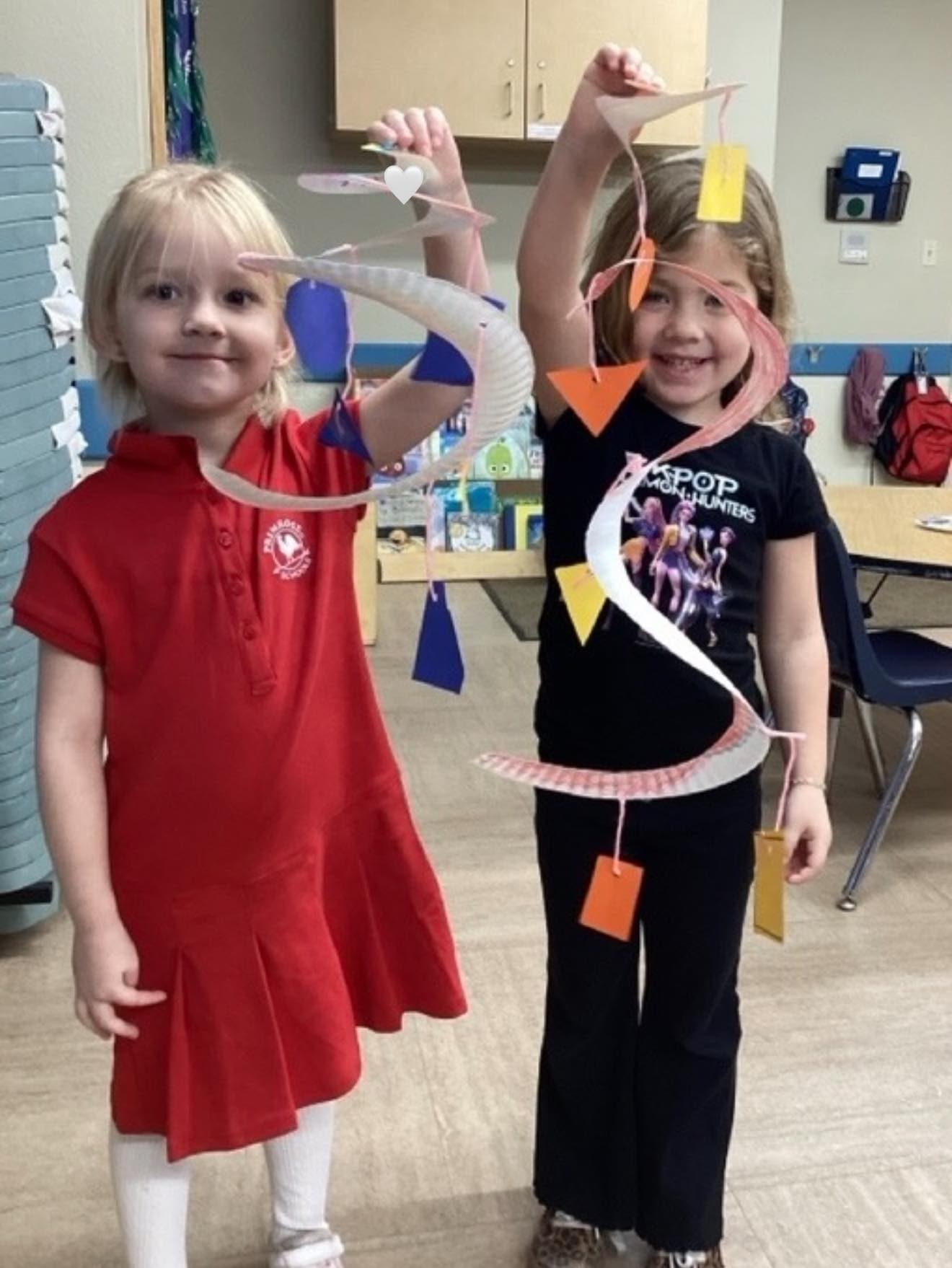 Two preschool children proudly displaying colorful paper mobiles they created during a hands-on art and design activity.