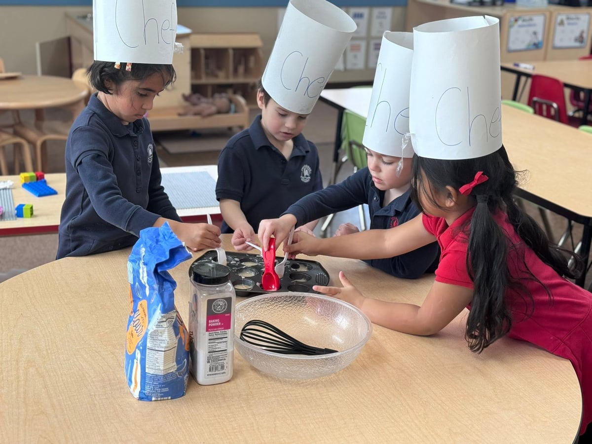 Preschool children wearing chef hats and working together to measure, mix, and prepare ingredients during a hands-on cooking activity that builds teamwork, math, and life skills at Primrose School.