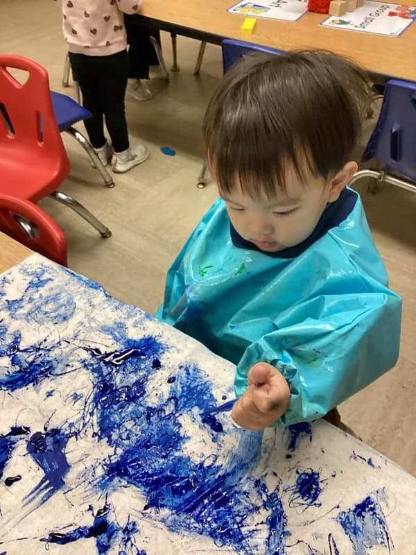 Toddler using paint-covered hands to explore textures, colors, and artistic expression during a hands-on classroom art project.