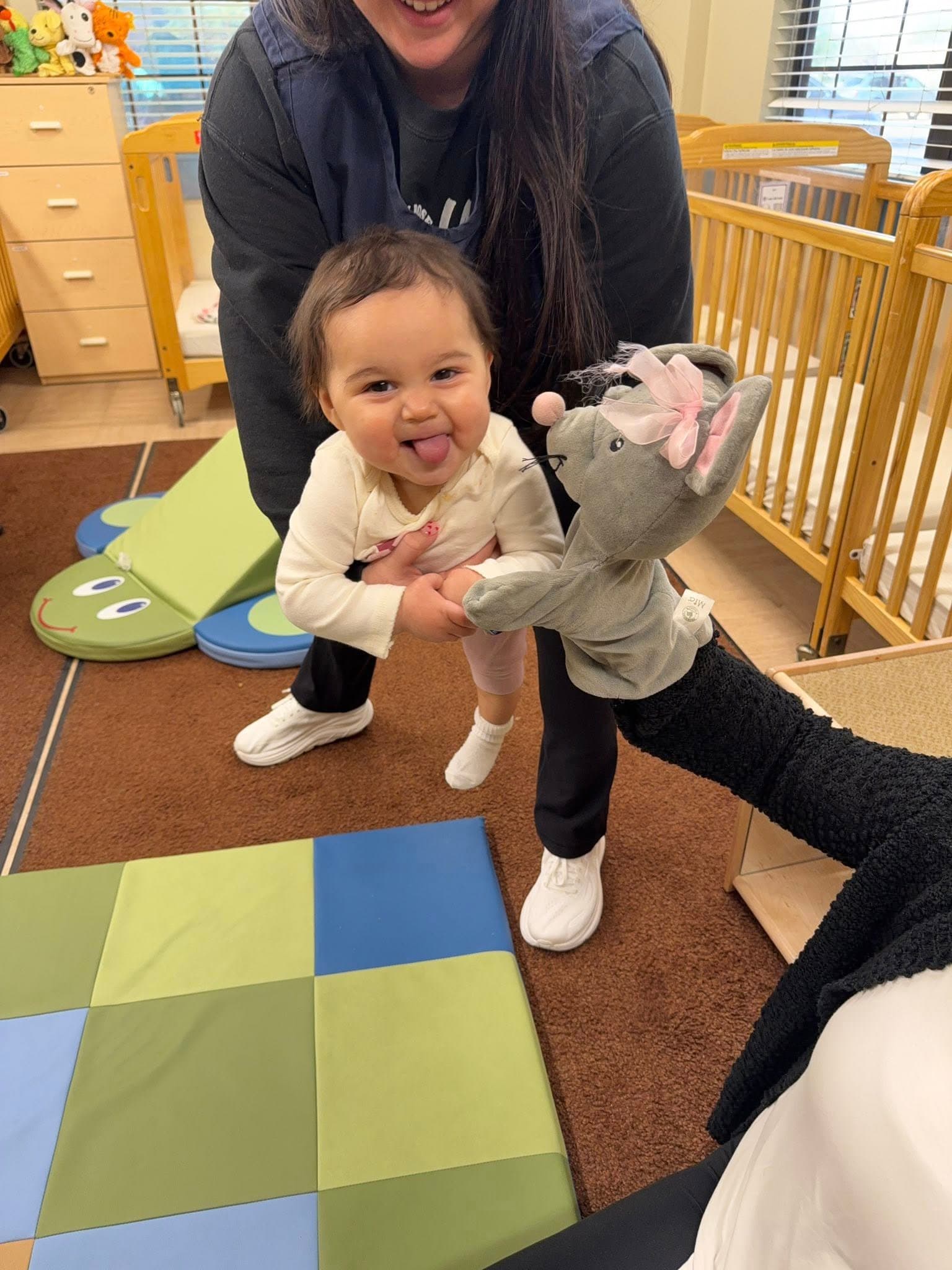 Infant smiling and interacting with a puppet during a playful classroom activity that encourages social engagement and early communication skills.