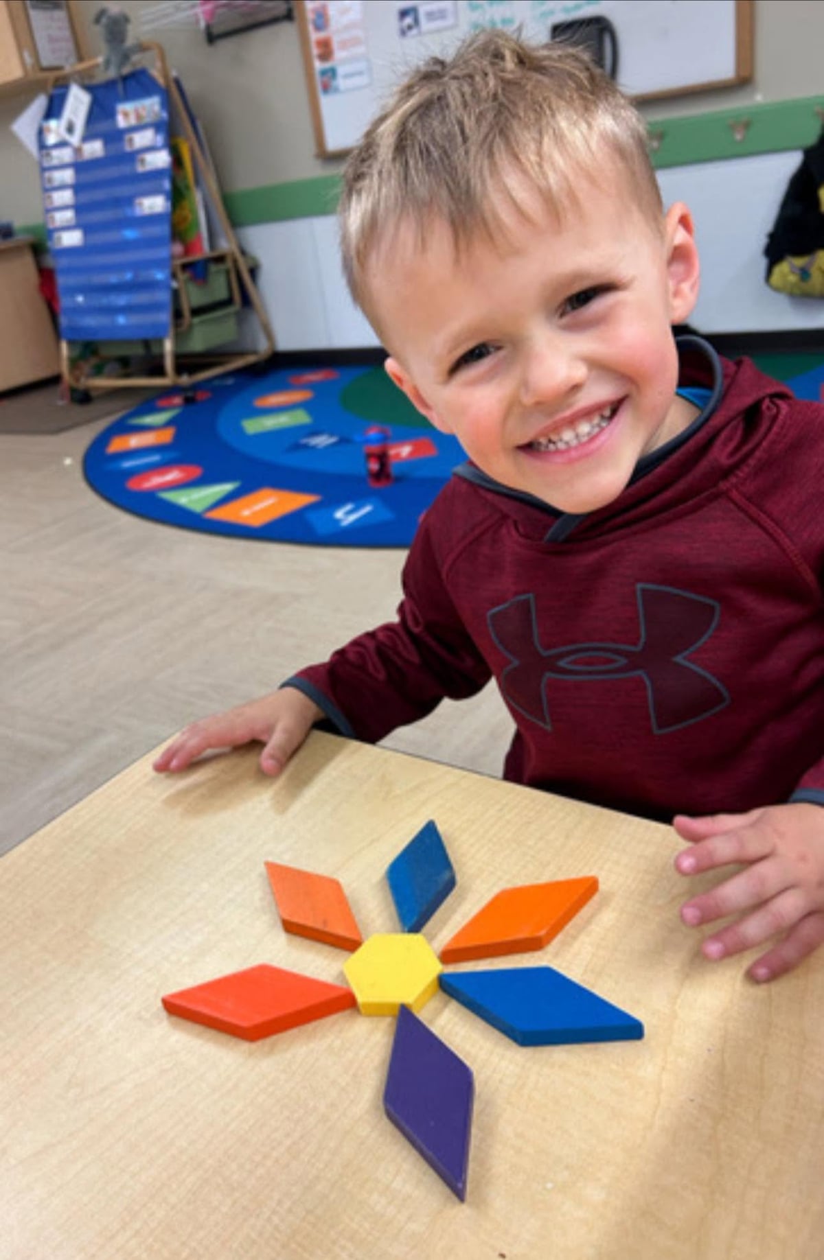 Smiling preschooler creating a flower design with colorful pattern blocks during a math activity that develops spatial awareness, geometry, and problem-solving skills at Primrose School.