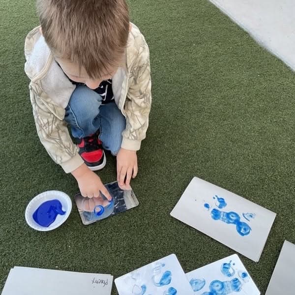 Child creating blue paint prints outdoors using hands-on stamping techniques that encourage creativity, sensory exploration, and artistic expression.