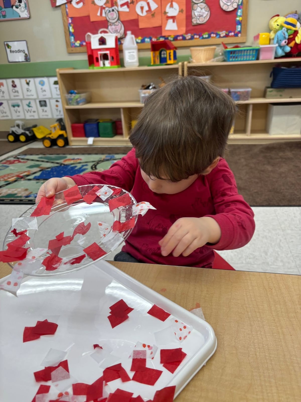 Toddler placing colorful tissue paper pieces onto a clear art project during a classroom activity that builds creativity, hand-eye coordination, and fine motor development at Primrose School.