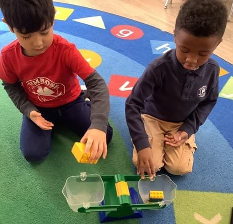 2 boys using a balance scale to compare the weight of 2 objects