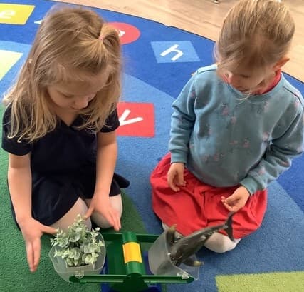 2 girls using a balance scale to compare the weight of 2 objects