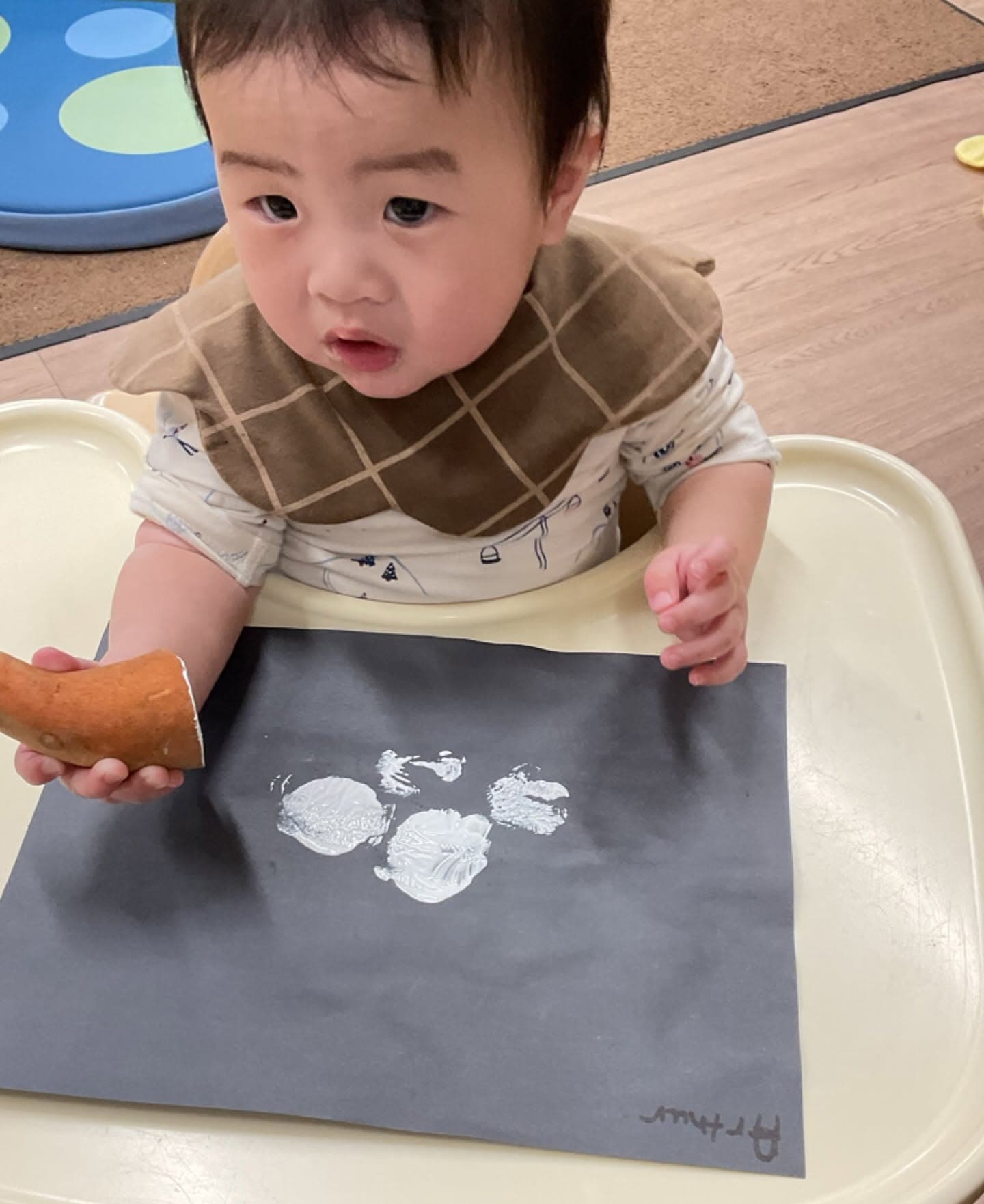 Infant using a paint stamper to create artwork on black paper while exploring colors, textures, and creativity during a classroom art activity.