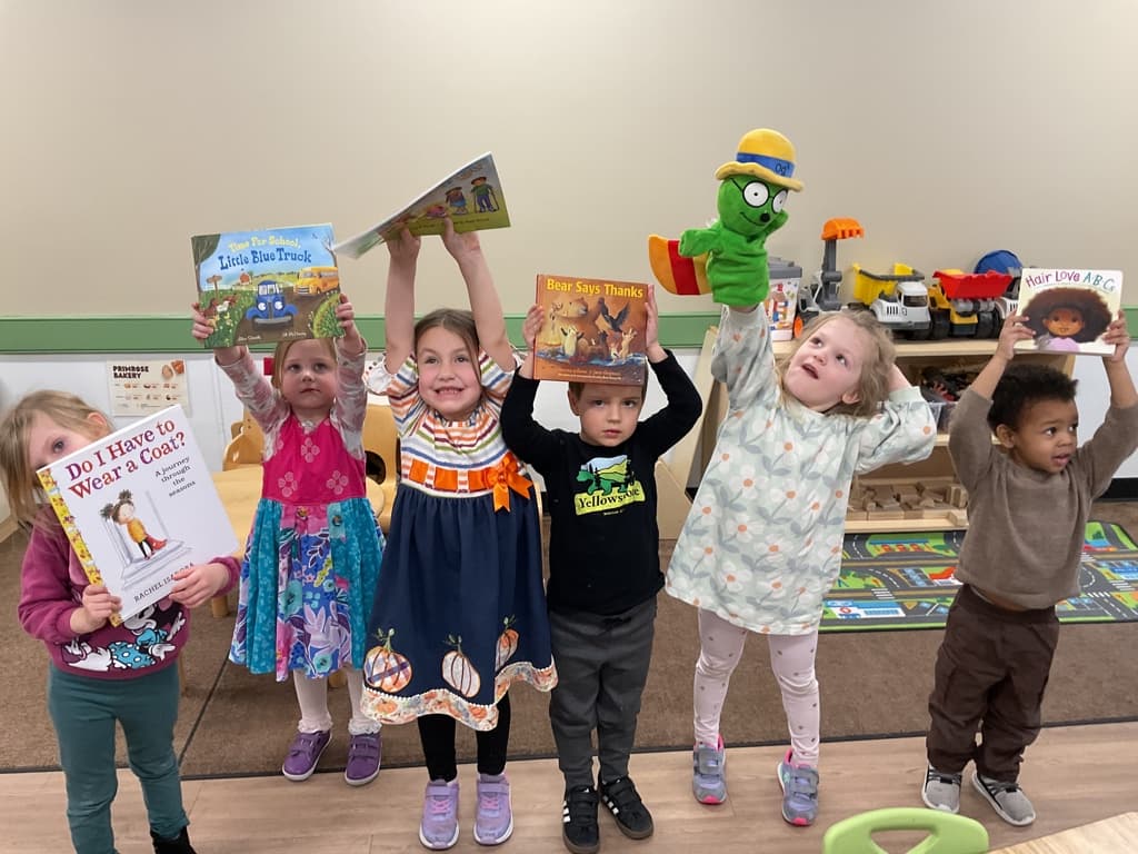 6 children holding up books and Og the bookworm puppet