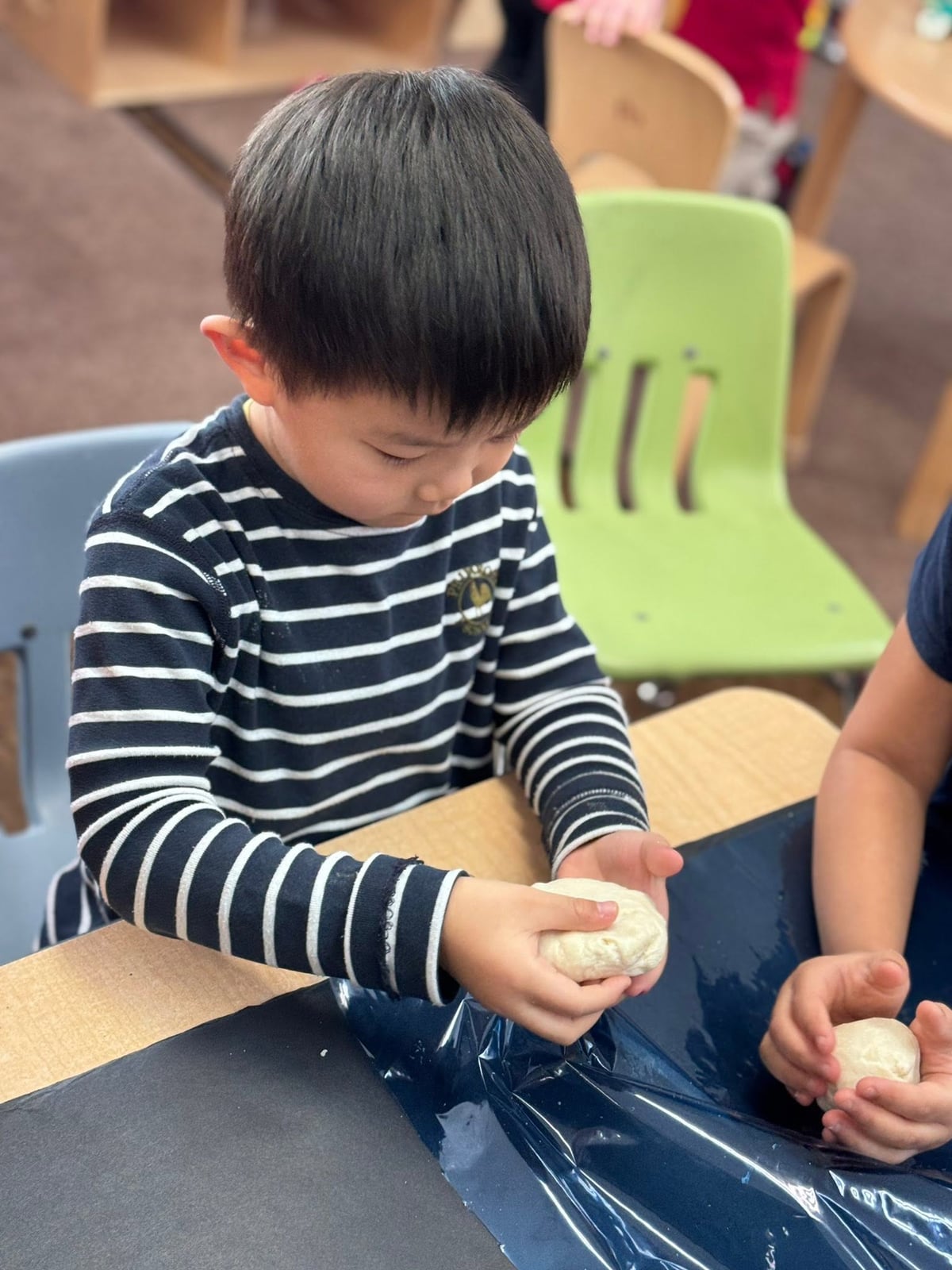 Preschooler squeezing and molding homemade dough to build hand strength, sensory awareness, and fine motor skills during a hands-on learning activity at Primrose School.