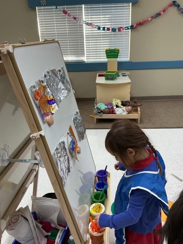 Preschool student painting at an easel while exploring colors, creativity, and fine motor development during an art activity at Primrose School.