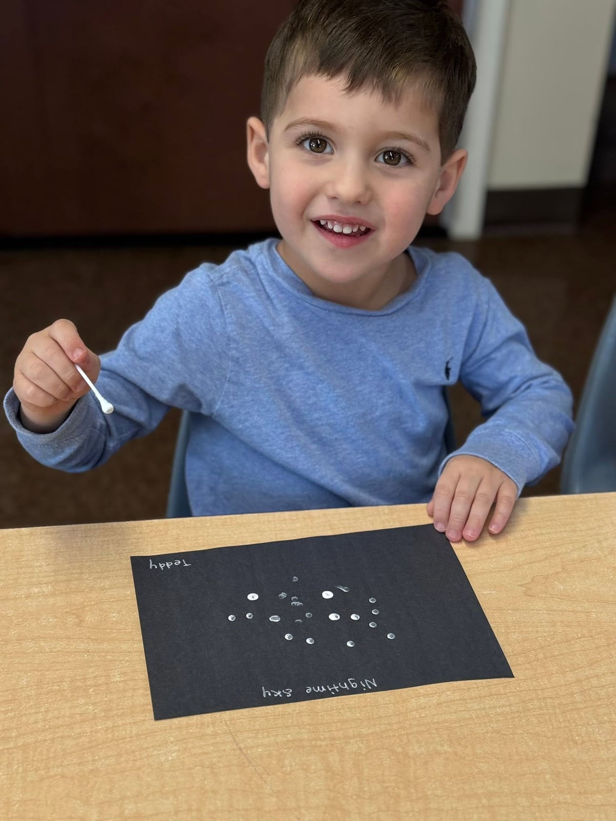 Preschooler using a cotton swab to create a starry night sky painting while strengthening fine motor skills, creativity, and artistic expression at Primrose School.