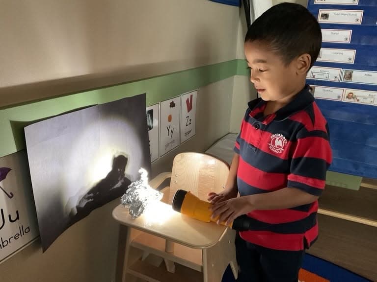 Young learner using a flashlight to investigate shadows and light patterns during a STEM activity that encourages scientific thinking and discovery.