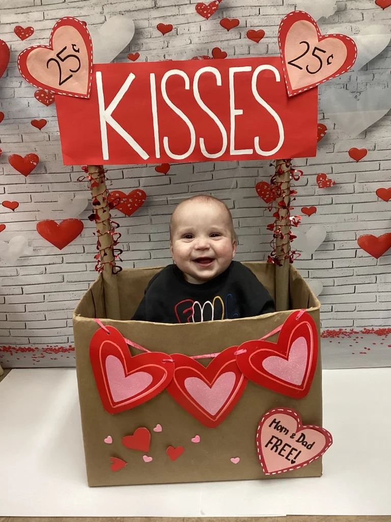 child sitting in box with hearts and it says kisses