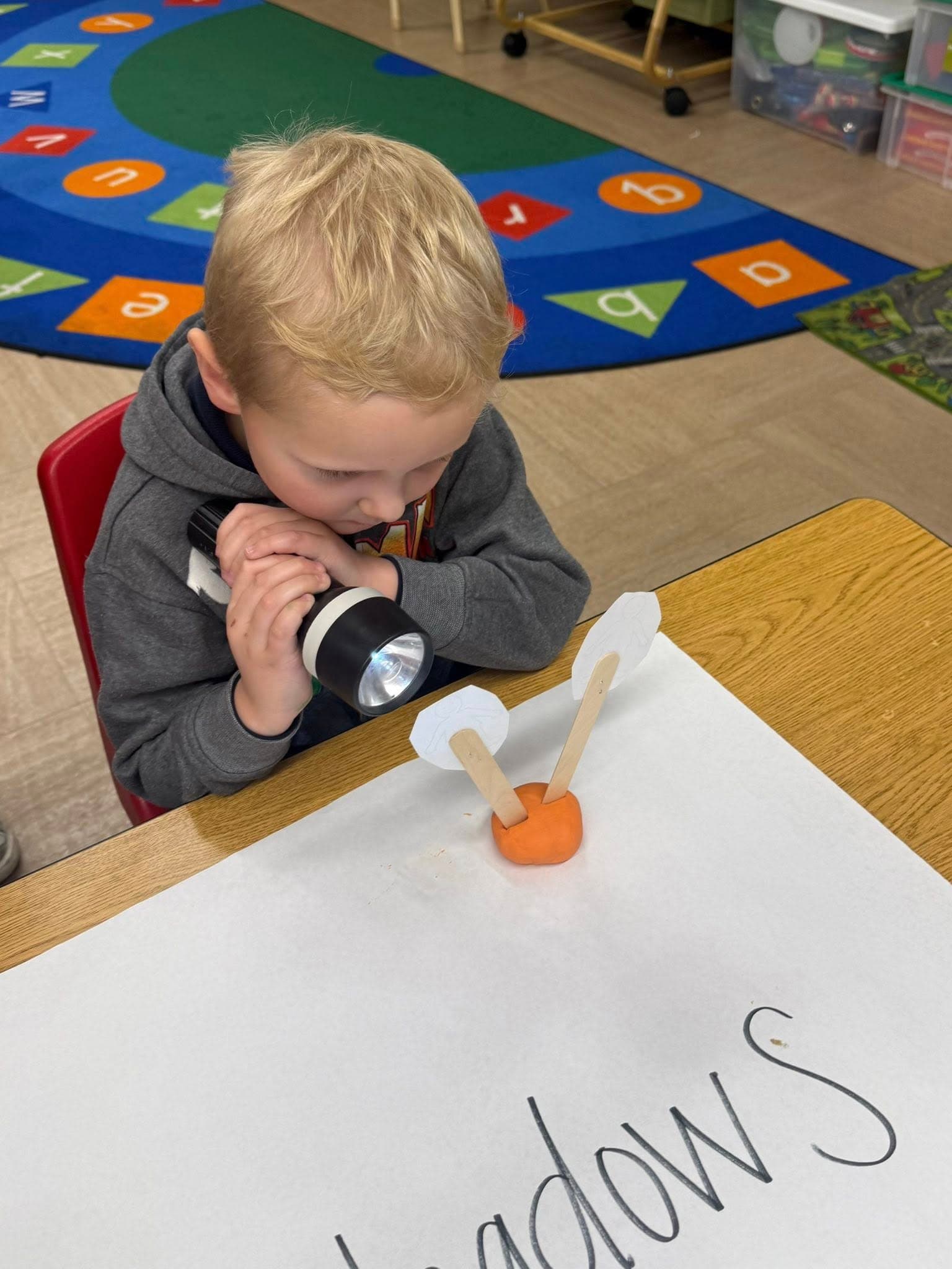 Preschool child using a flashlight to explore shadows during a hands-on science investigation.