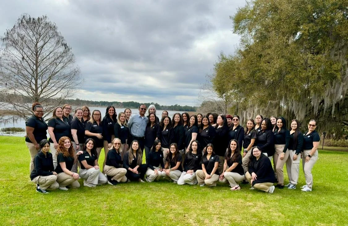 women in black polos and khaki pants on the grass in front of a lake