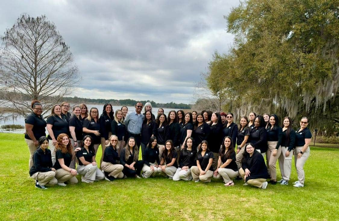 women in black polos and khaki pants on the grass in front of a lake