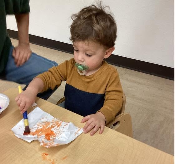 Toddler using a paintbrush to create artwork during a hands-on art activity that encourages creativity and fine motor development at Primrose School.
