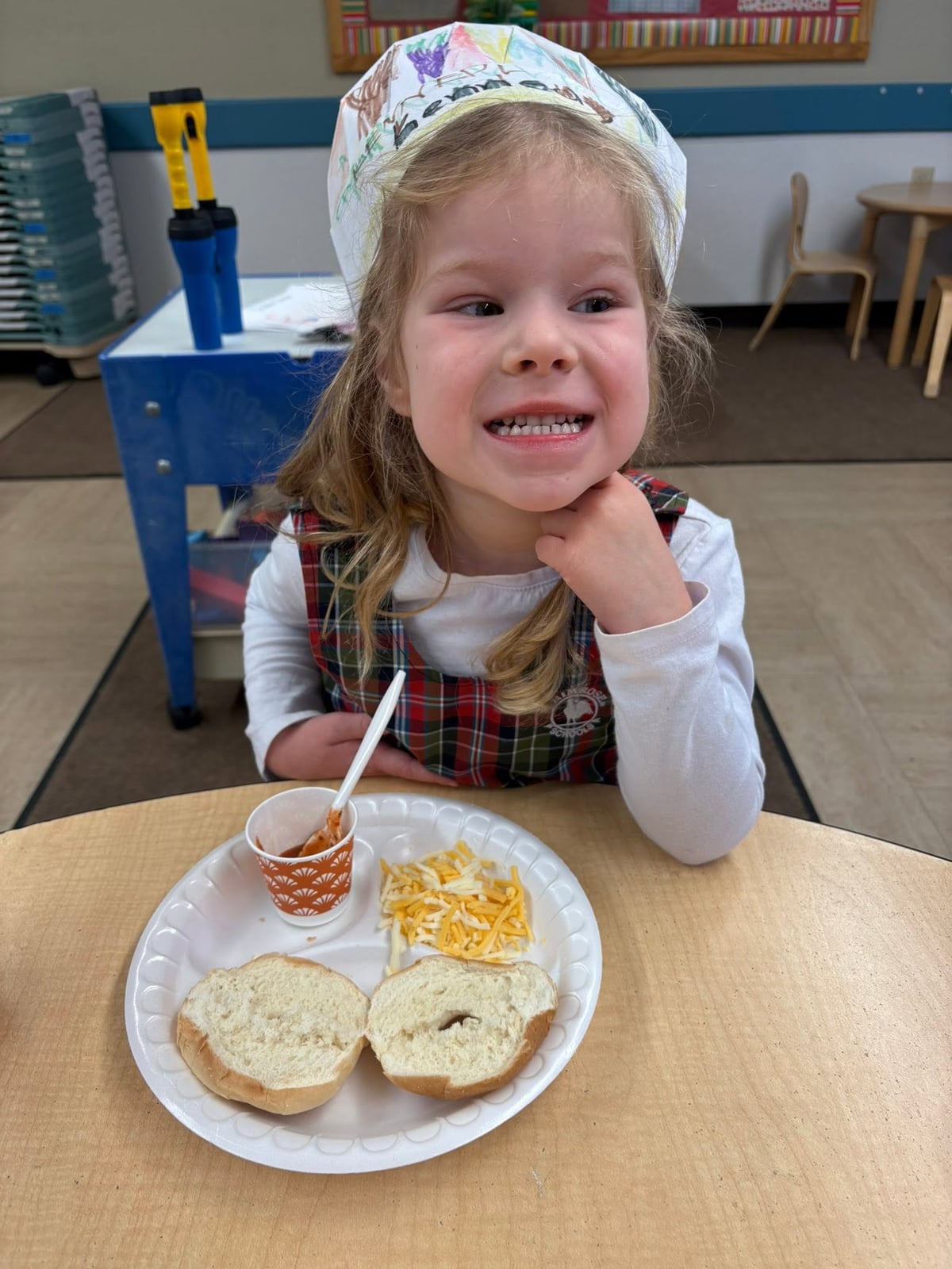 Preschool student smiles while making a bagel snack during a hands-on cooking activity at Primrose School.