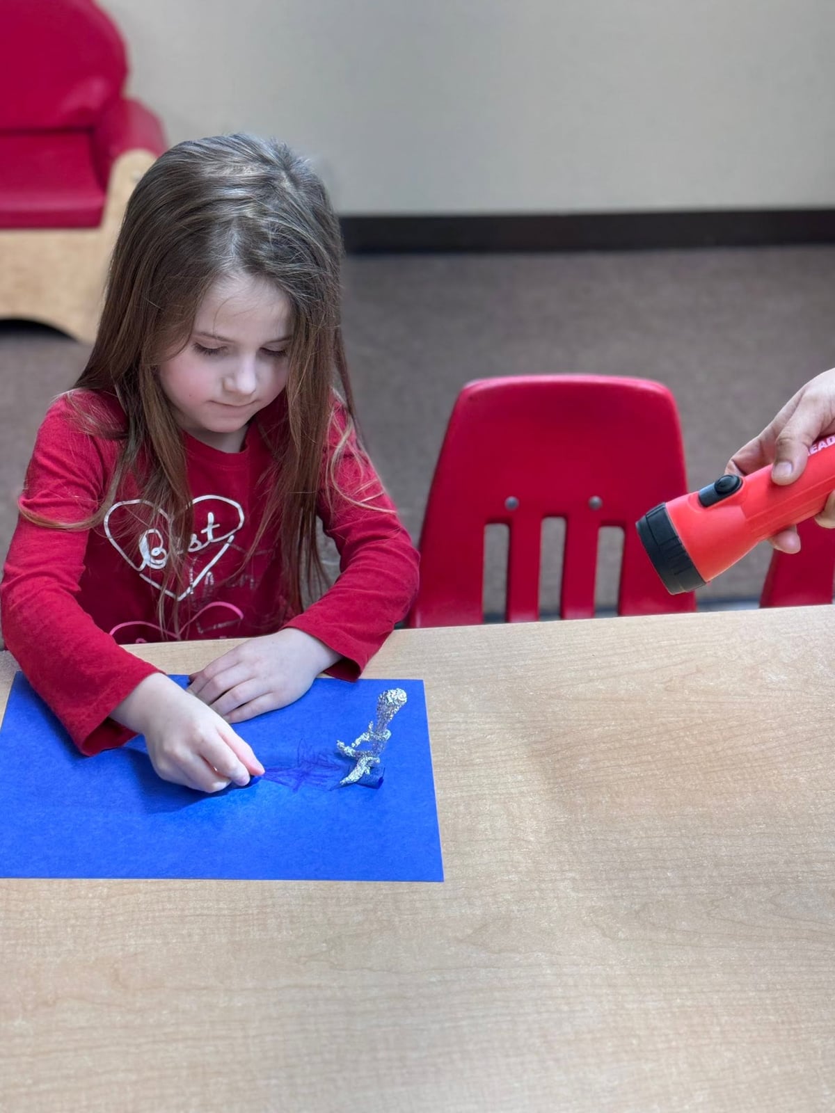Preschooler using a flashlight to explore shadows and create artwork while building observation, scientific thinking, and creativity during a STEAM activity at Primrose School.