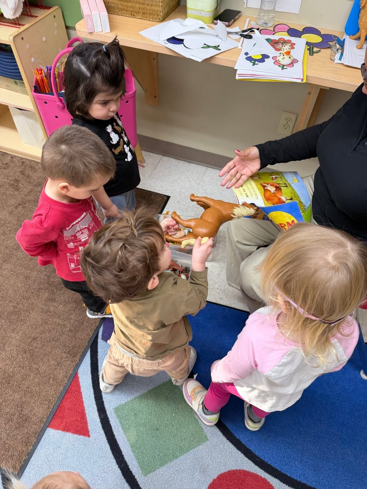 Toddlers gathered with their teacher to explore a storybook and animal figures during an interactive literacy activity that encourages language development, listening skills, and curiosity at Primrose School.