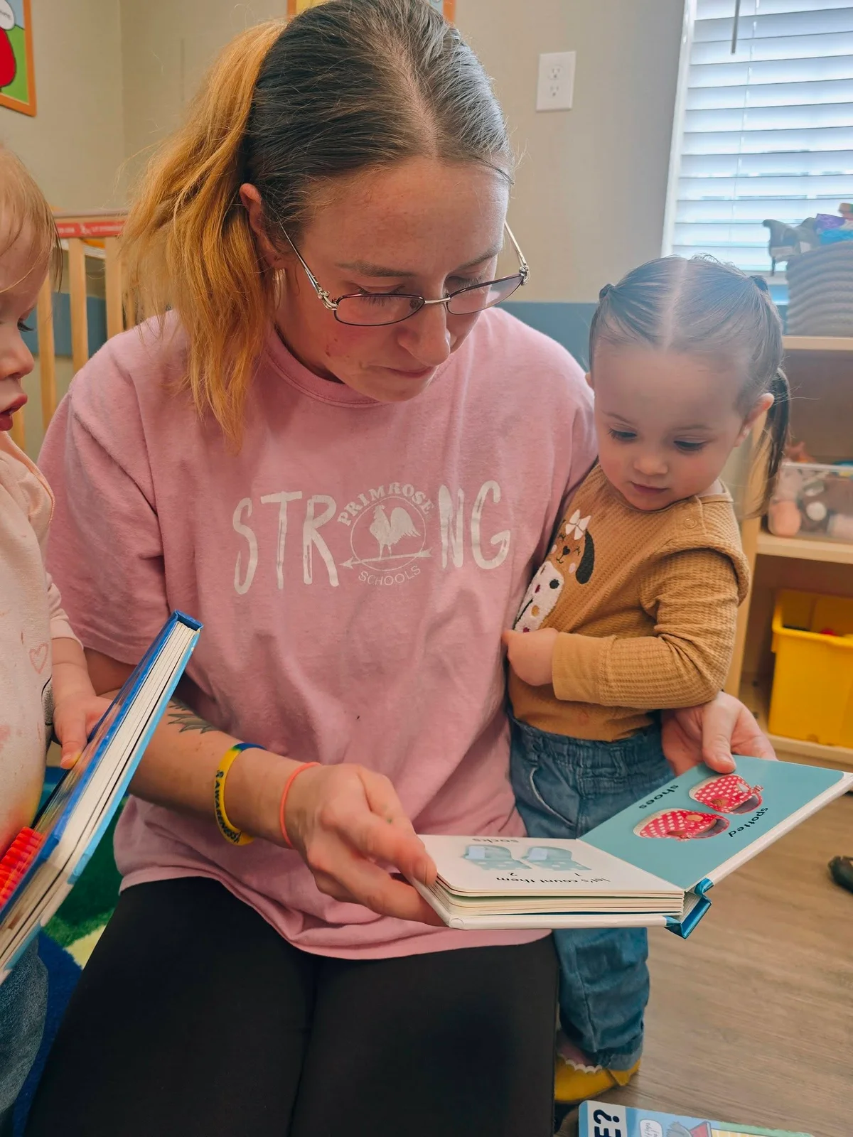 Teacher and toddler girl reading a book together in a daycare classroom in Keller, TX.