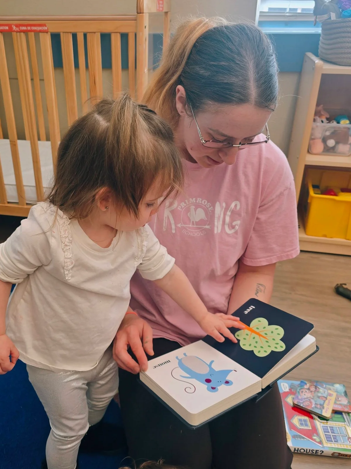 Teacher and toddler girl reading a book together in a daycare classroom in Keller, TX.