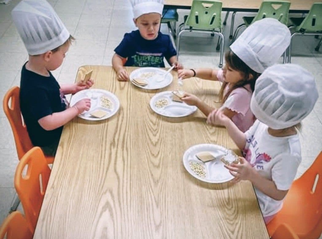 Young children wearing chef hats while participating in a classroom cooking activity that encourages teamwork, creativity, and life skills.