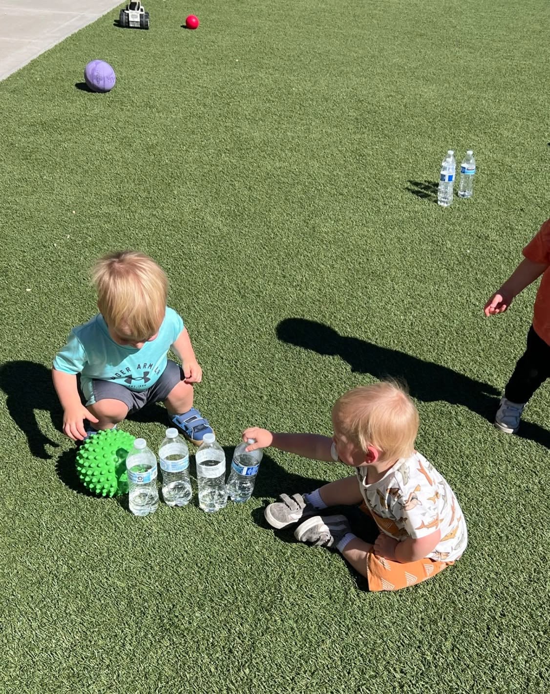 Toddlers exploring water bottles and textured play equipment during an outdoor activity that promotes curiosity, movement, and sensory learning at Primrose School.
