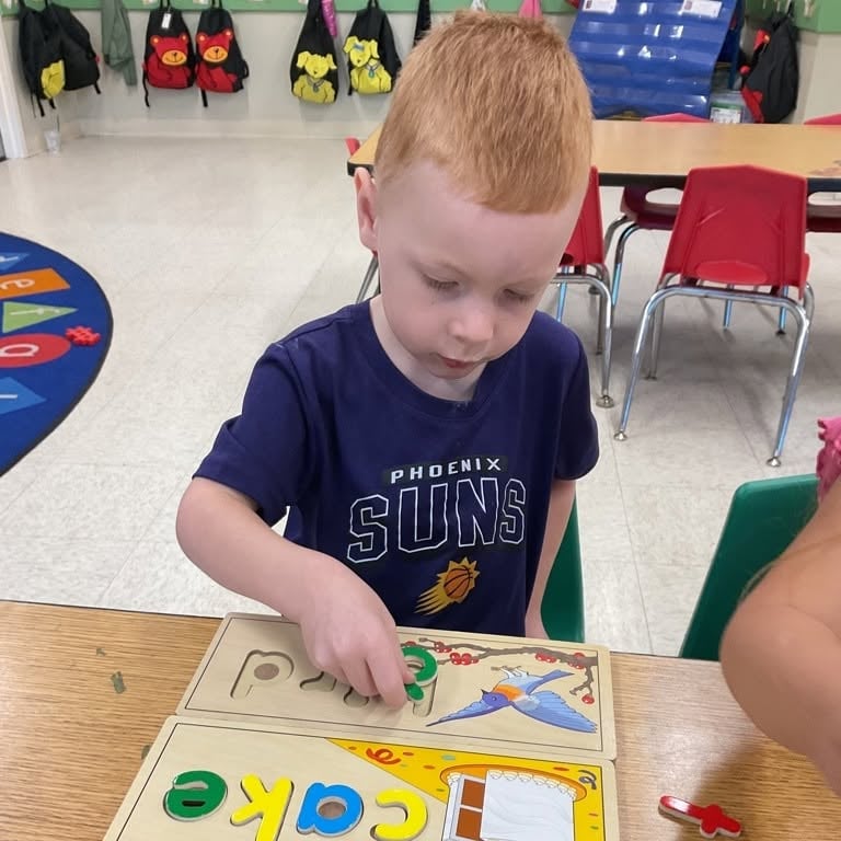 Preschool student matching letters with a wooden alphabet puzzle to build letter recognition, fine motor skills, and early literacy foundations at Primrose School.