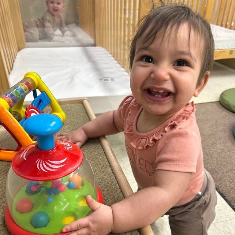 Smiling infant exploring a colorful cause-and-effect toy that encourages fine motor development, hand-eye coordination, sensory exploration, and early problem-solving skills at Primrose School.