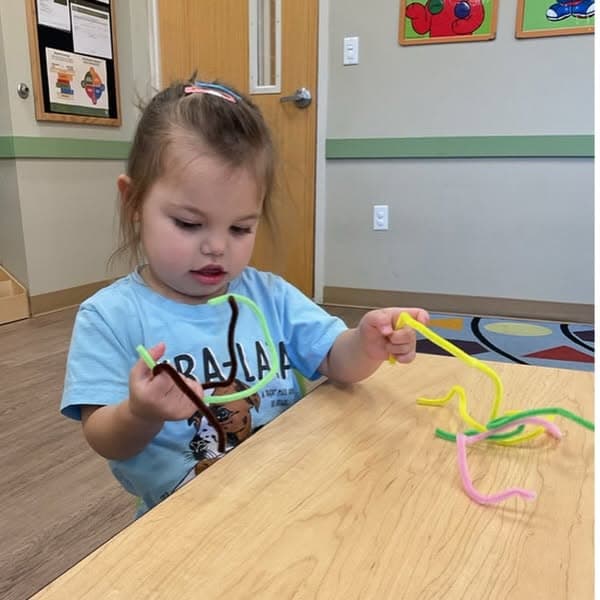 Toddler manipulating colorful pipe cleaners during a classroom activity designed to build hand-eye coordination, dexterity, and problem-solving skills.