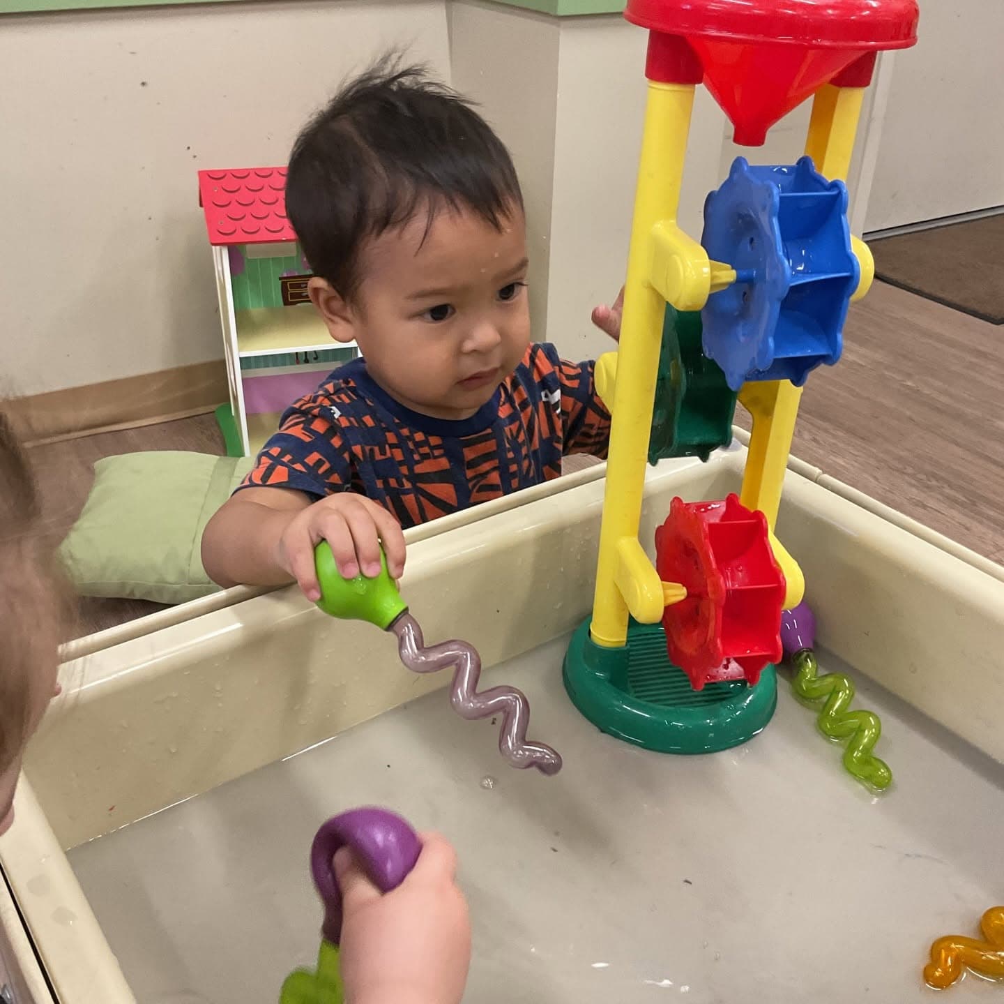 Toddler engaging in sensory water play with interactive tools and water wheels, developing fine motor skills, cause-and-effect understanding, and scientific exploration.